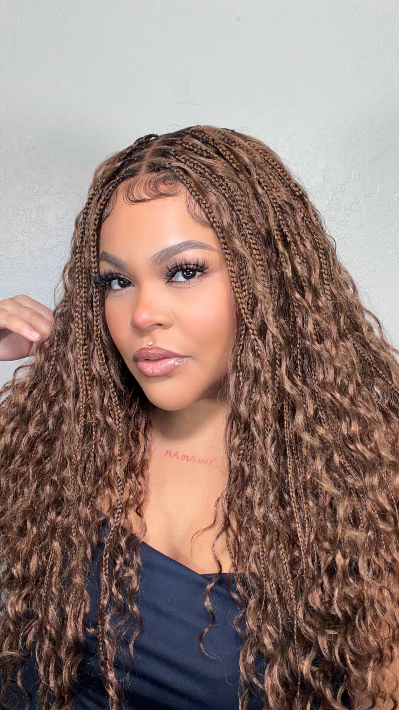 Woman with long, wavy, brown boho knotless wig hair against a plain background